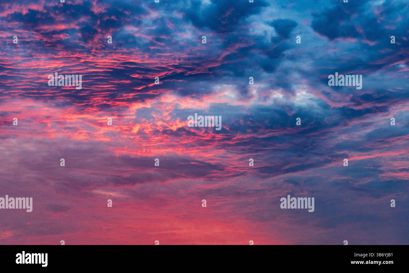 Ein atemberaubender Himmel voller lebendiger Farben während des Sonnenuntergangs, der eine Mischung aus Rosa, Lila und Blau zwischen strukturierten Wolken zeigt. Stockfoto