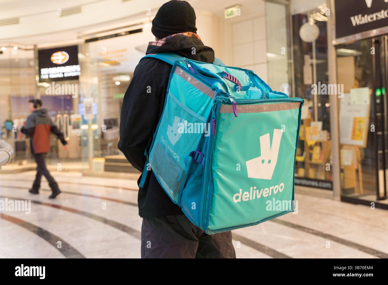 Deliveroo Fahrer holt die Mitnahme des Kunden in seiner Tasche vom Restaurant in der Shopping Mall in London, Großbritannien Stockfoto