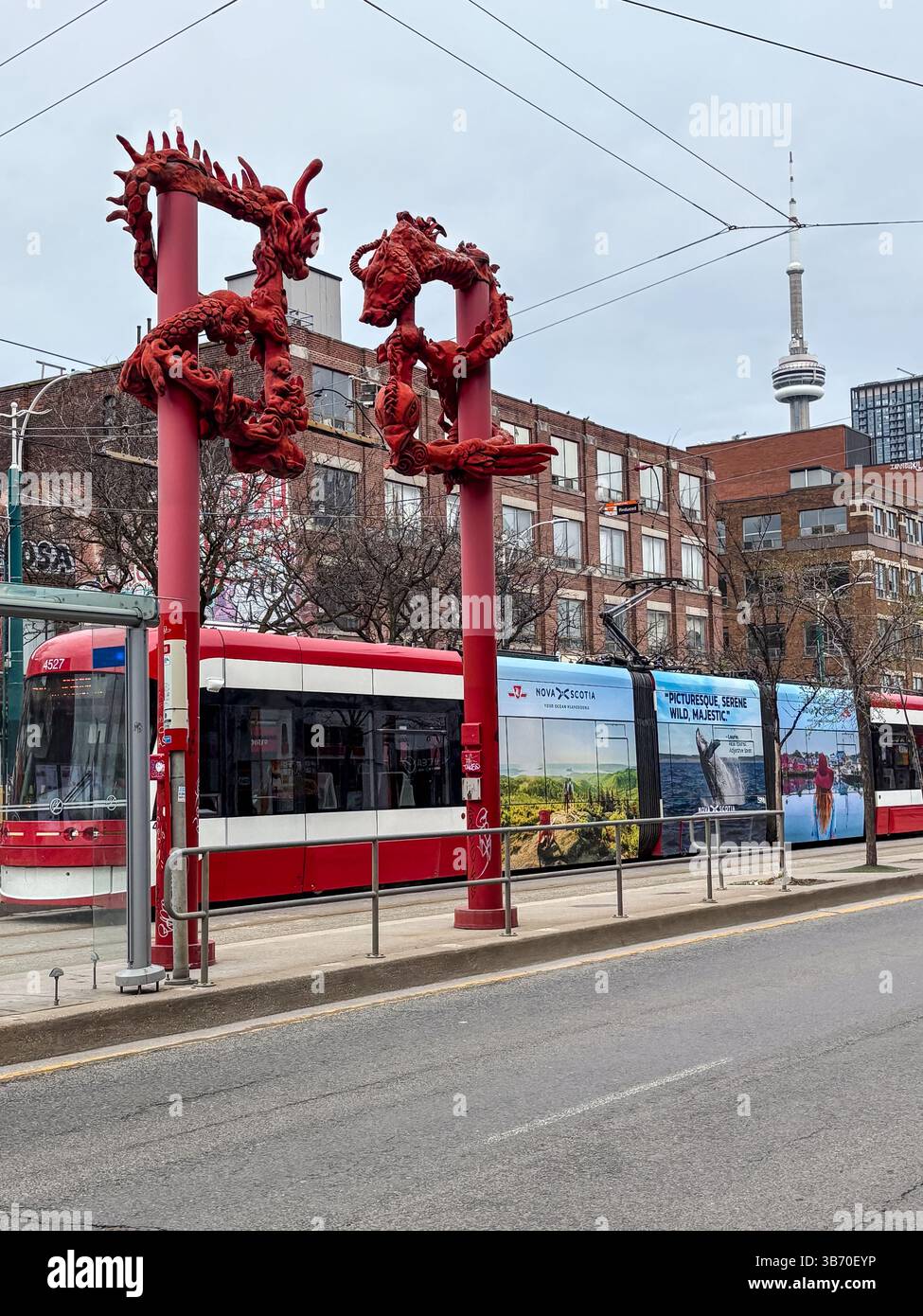 Toronto Chinatown Torbogen mit einer roten TTC-Straßenbahn, die vorbeifährt. Der CN Tower ist an einem bewölkten Tag im Hintergrund sichtbar. Urbane Straßenszene in Stockfoto