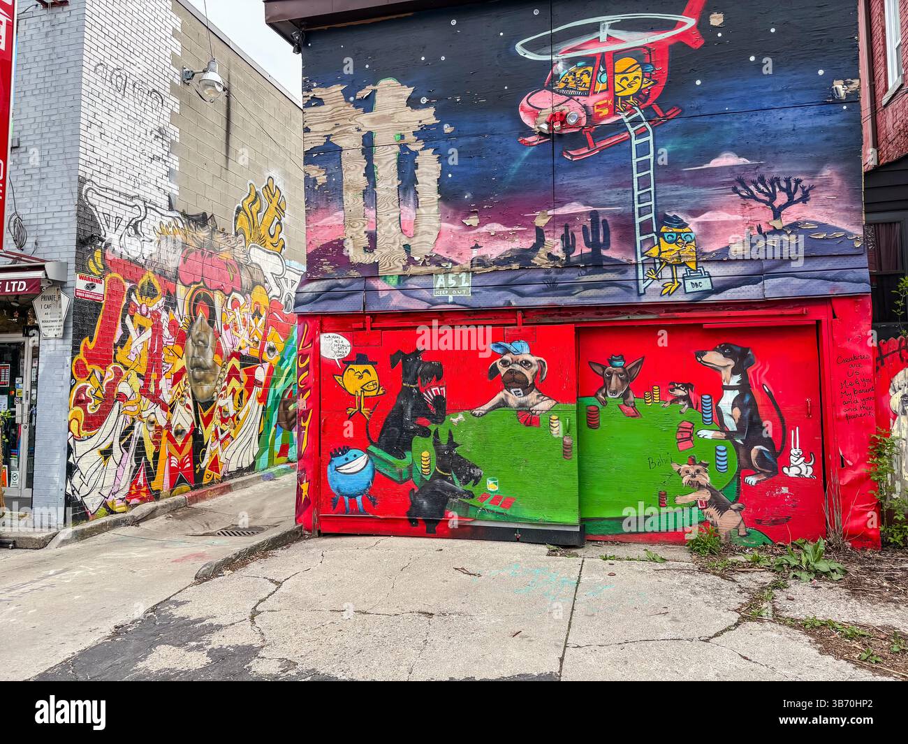 Graffiti-Gasse in Toronto, Kanada, mit einer Gebäudewand, die mit farbenfroher Straßenkunst bedeckt ist, einschließlich eines Wandgemäldes mit Poker spielenden Hunden und einem Hubschrauber. Stockfoto