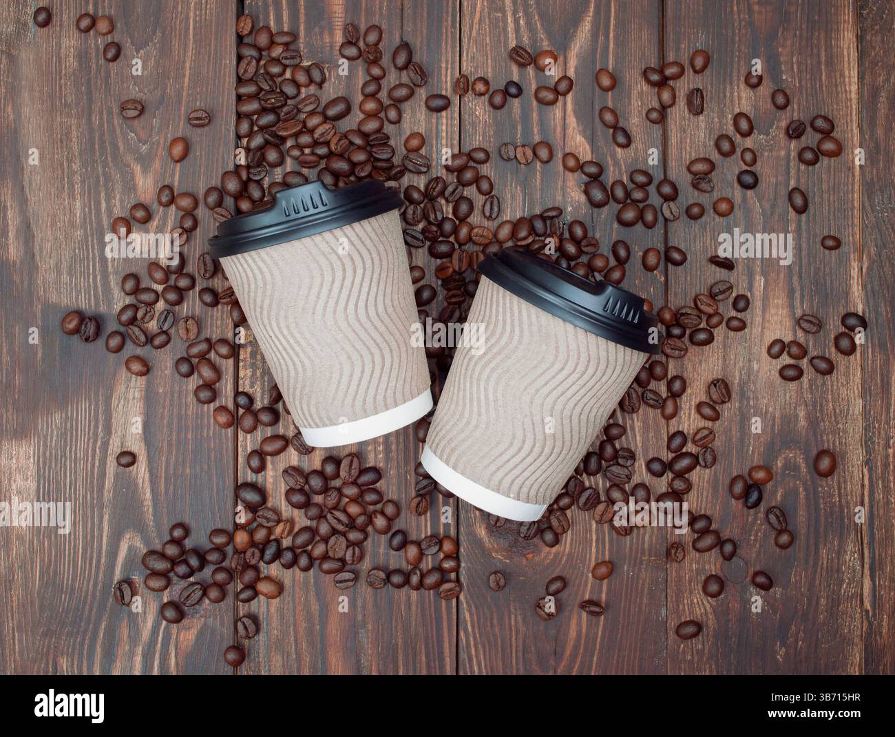 Aromatische geröstete Kaffeebohnen mit nachgebildeter Papiertasse zum Mitnehmen. Dunkler Hintergrund, Draufsicht, Copyspace. Stockfoto