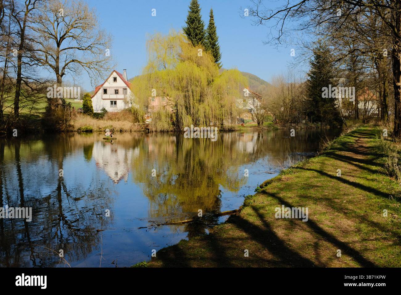 Dorfhäuser mit bunten Bäumen, die sich im Frühling in einem ruhigen See unter blauem Himmel in ländlicher europäischer Umgebung spiegeln. Hochwertige Fotos Stockfoto