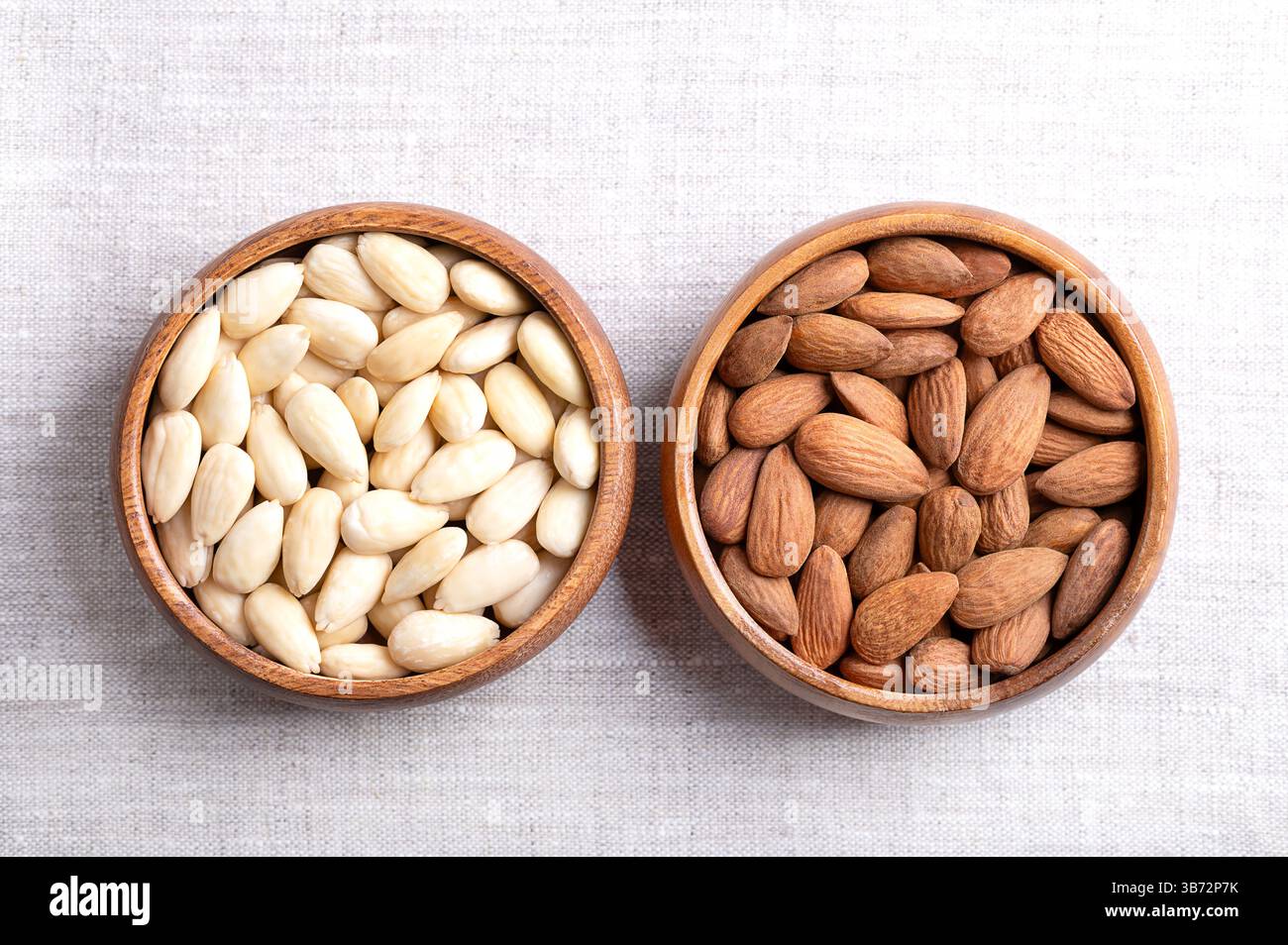 Mandeln mit Haut und hautlose Mandeln in Holzschalen auf Leinen. Früchte von Prunus amygdalus, syn. Prunus dulcis, mit Samenmänteln und blanchiert. Stockfoto