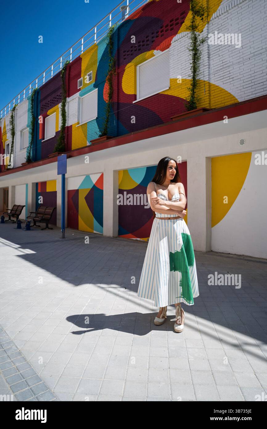 Stilvolle Frau posiert selbstbewusst vor einer lebendigen, geometrisch bemalten Wand und zeigt urbane Mode und farbenfrohe Street Art Stockfoto