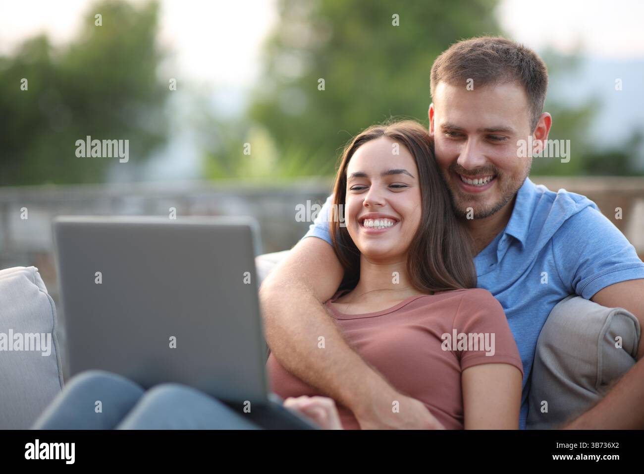 Glückliches Paar, das zu Hause auf einem Sofa auf einer Terrasse auf dem PC sitzt Stockfoto