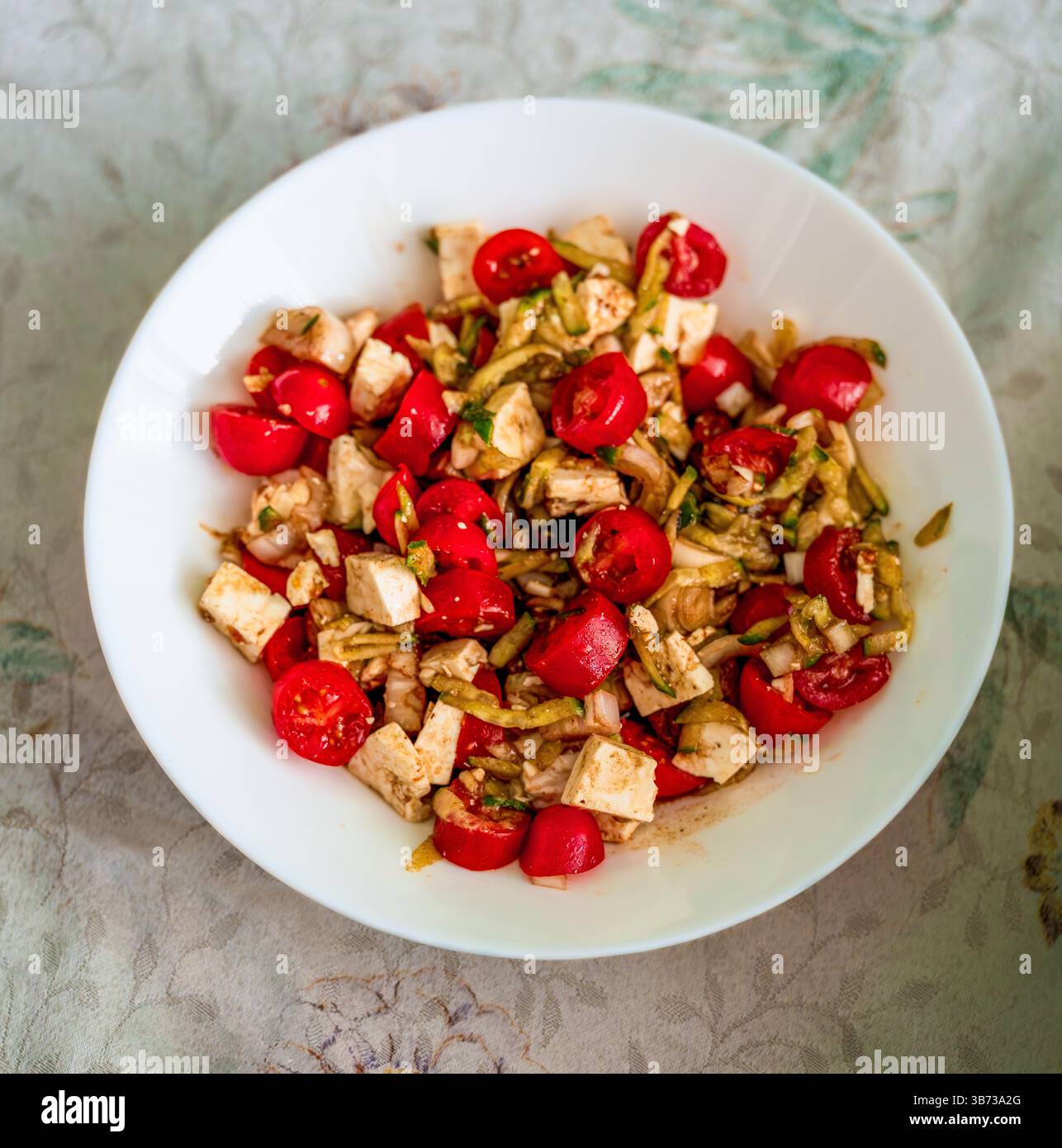 Knuspriger griechischer Salat aus Kirschtomaten, Fetakäsewürfeln, Gurkenbändern und roten Zwiebeln in Oregano-Öl Stockfoto