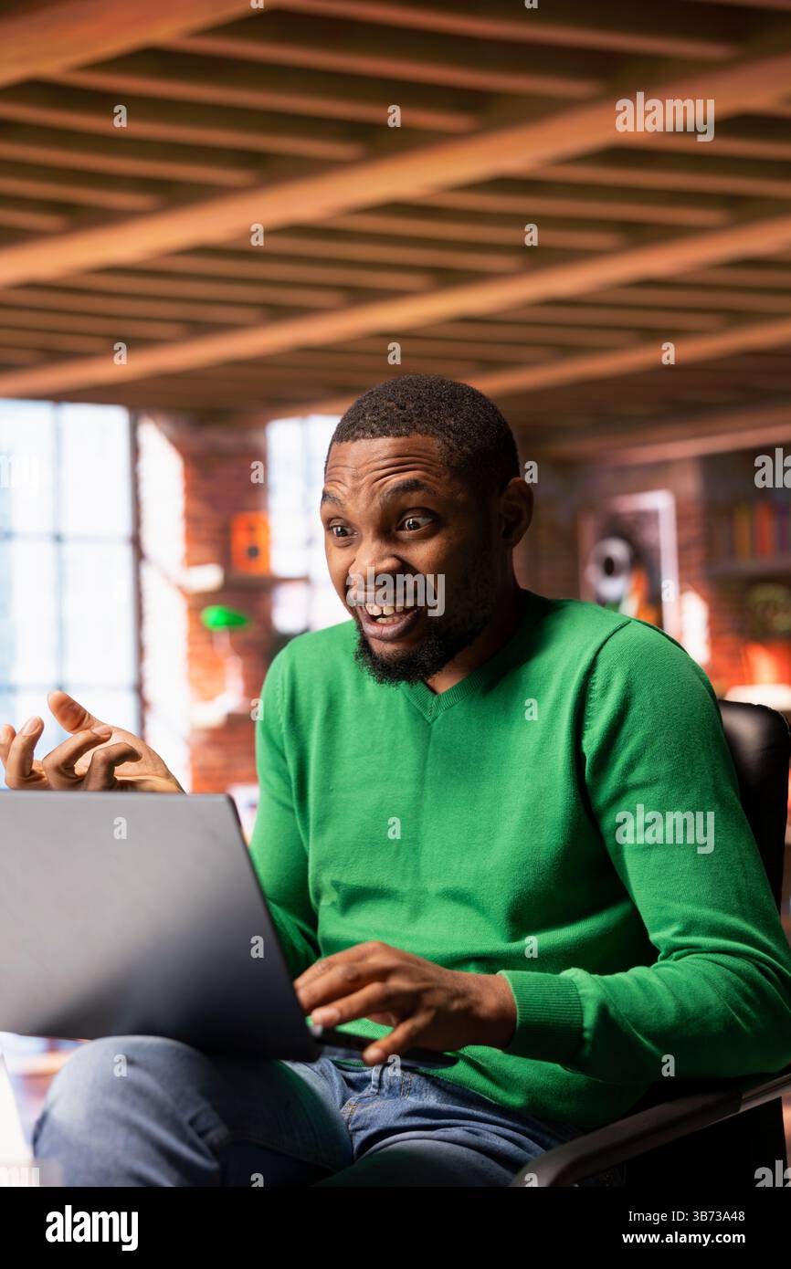 Ein aufgeregter Mann, der Fernsehsendungen auf einem Laptop ansieht, vertieft von atemberaubenden Ereignissen, sitzt am Rand des Sitzes. Eine begeisterte Person, die auf einem Stuhl in der Wohnung sitzt, überrascht von der schockierenden Drehung des Films Stockfoto