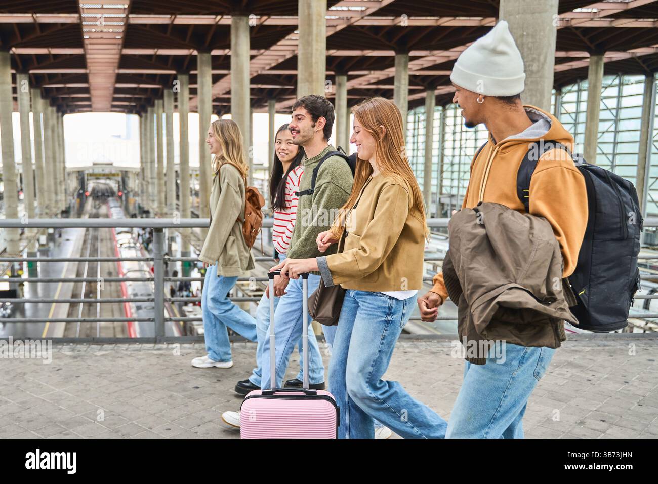 Gruppe junger Touristen, die gemeinsam im Bahnhof unterwegs sind, mit Gepäck und Rucksäcken, bereit für ihr nächstes Abenteuer Stockfoto