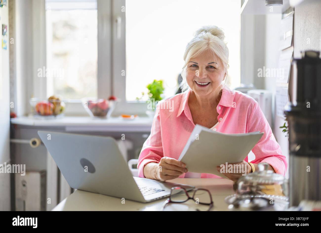 Frau, die mit Laptop und Dokumenten am Küchentisch zu Hause arbeitet Stockfoto