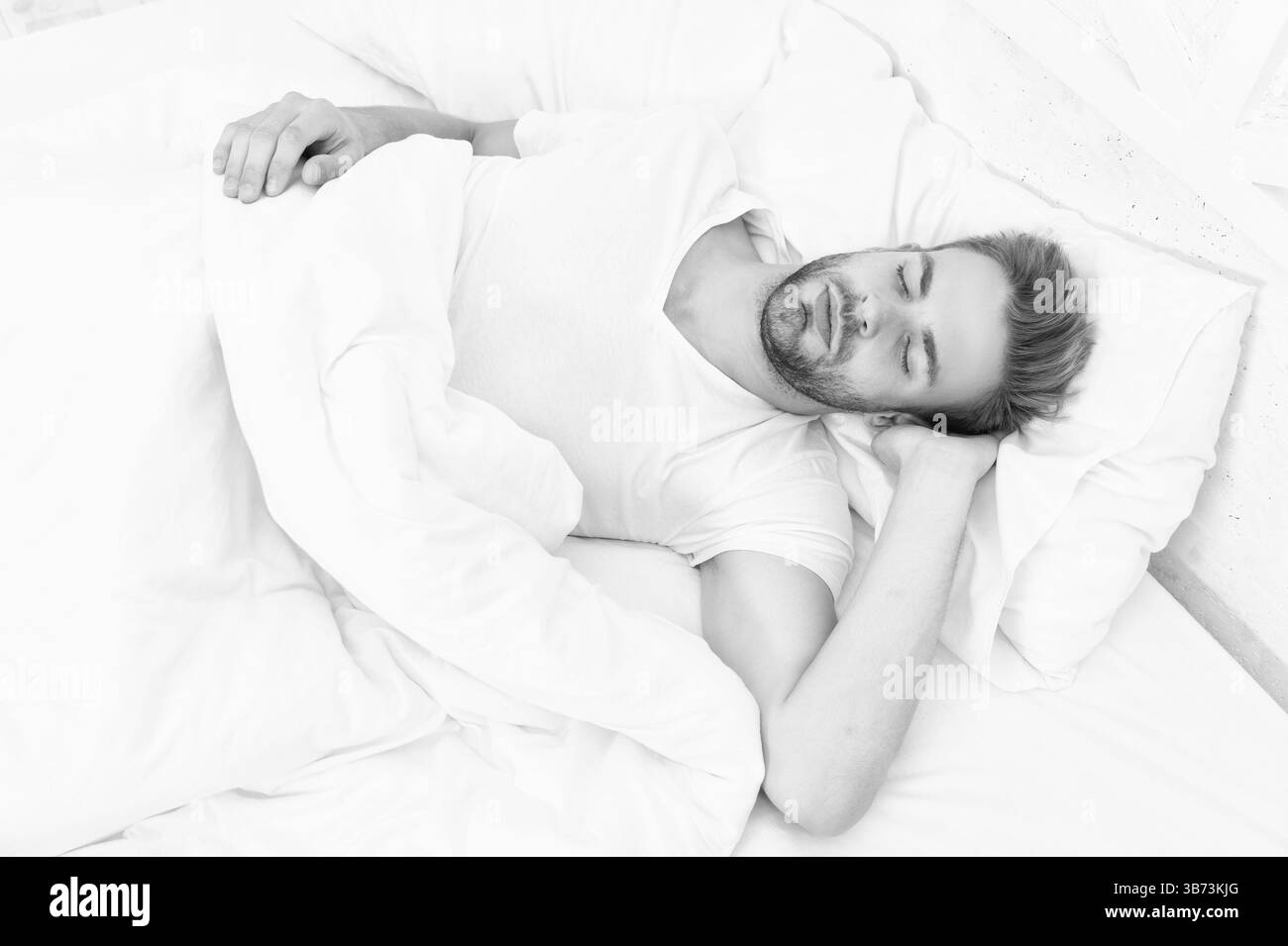 Mit geschlossenen Augen liegen. Tiefer Männerschlaf. Mann, der nachts schläft. Schläfriger Mann, der auf dem Bett liegt und im weißen Schlafzimmer schläft. Schlafender junger Mann, der schläft. Ruhezustand Stockfoto