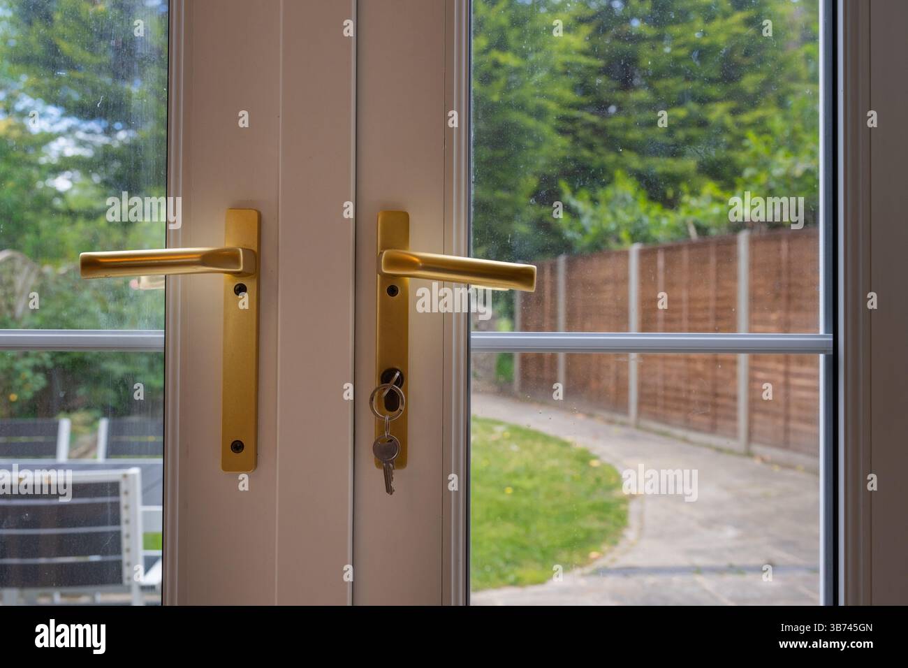 Detail der Terrassentüren mit Garten dahinter. Goldene Griffe mit Schlüssel in Schloss. Stockfoto
