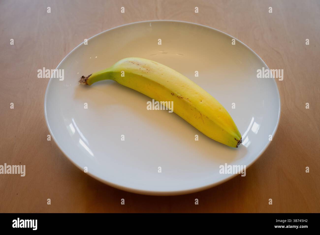 Eine frische Banane in einer weißen Schale auf einem Holztisch Stockfoto