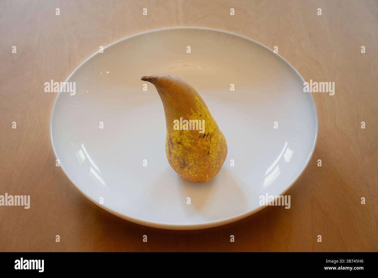 Eine Birne steht in einer weißen Schale auf einem Holztisch Stockfoto