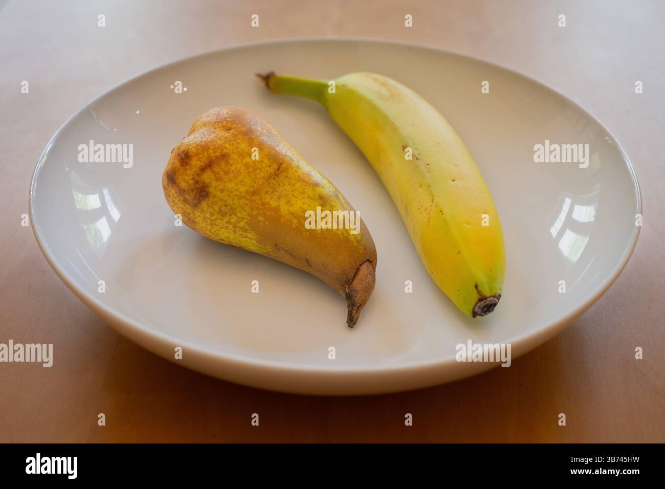 Eine Birne und eine Banane in einer weißen Schale auf einem Holztisch Stockfoto