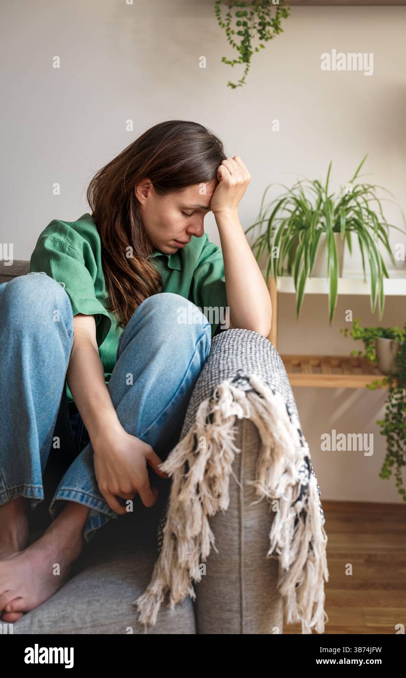 Ausgebrannte Frau, die auf dem Sofa sitzt und den Kopf auf der Hand hält Stockfoto