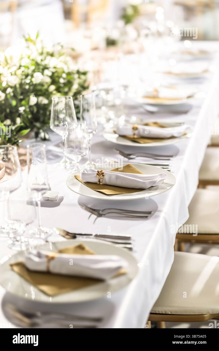 Ein Hochzeitstisch mit einer weißen Tischdecke, dekoriert mit Blumen, Kerzen, Gläsern und Besteck. Stockfoto
