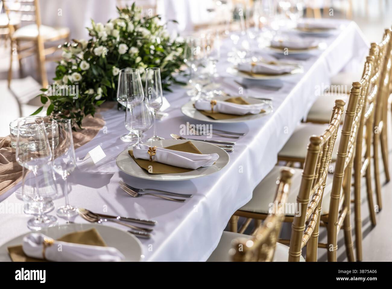 Ein Hochzeitstisch mit einer weißen Tischdecke, dekoriert mit Blumen, Kerzen, Gläsern und Besteck. Stockfoto