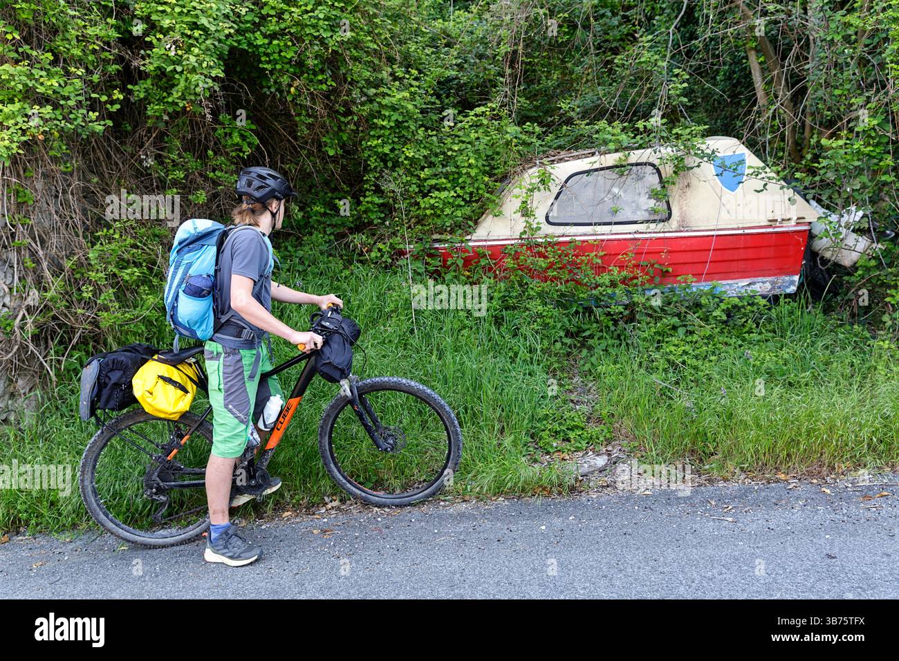 Radfahrer auf einem Mountainbike beobachtet verlassenes Boot in einem kleinen Dorf in Podpec, Slowenien, touristische Radtouren in Slowenien Stockfoto