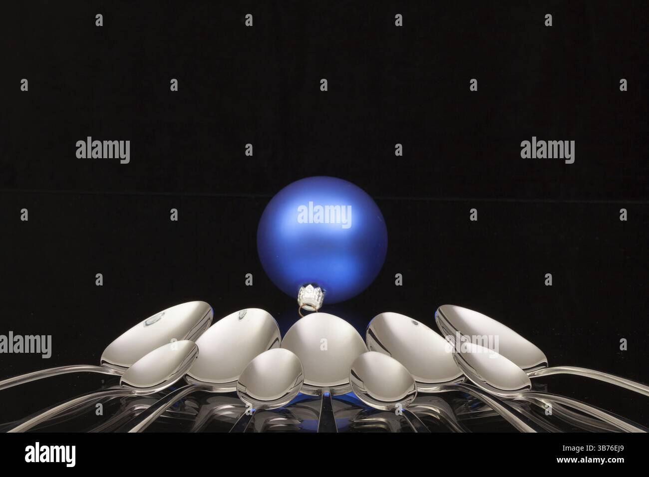 Blaue Weihnachtsdekoration und neun Löffel auf einem Schreibtisch Schwarzglas Stockfoto