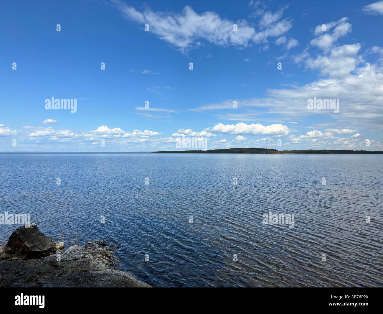 Eine wunderschöne Landschaft eines ruhigen Sees unter einem leuchtend blauen Himmel mit flauschigen Wolken. - Smartphone-aufgenommenes Stockfoto