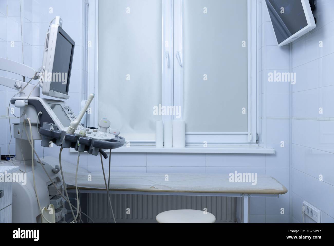 Das Bild zeigt einen sterilen medizinischen Ultraschallraum, der mit moderner Technologie ausgestattet ist und einen Bestrahlungstisch, einen Monitor und ein Fenster zur Hervorhebung aufweist Stockfoto