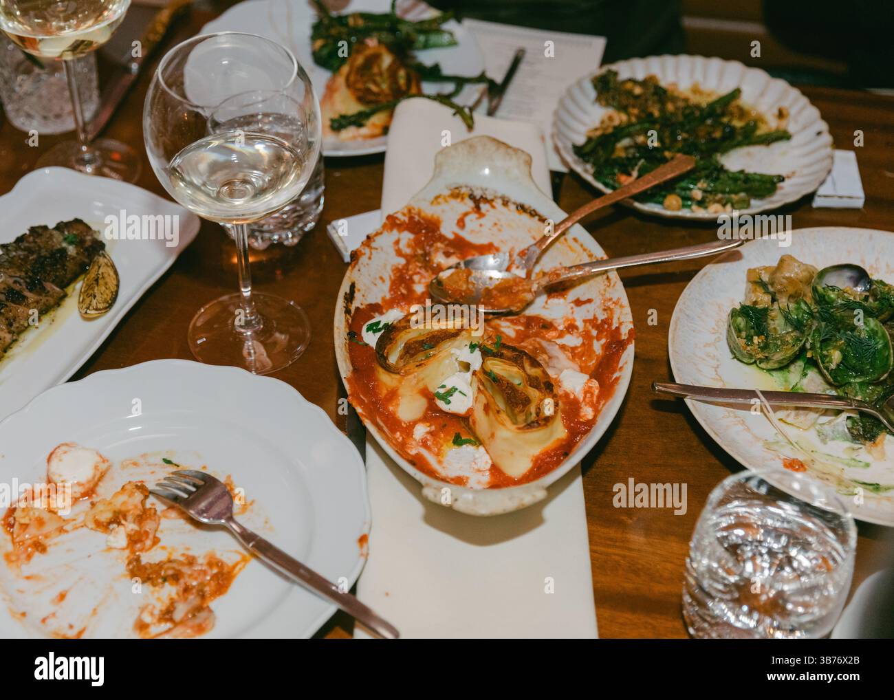 Gäste genießen eine Vielfalt an Gerichten und Wein in einer warmen, einladenden Umgebung, die ein gemeinsames kulinarisches Erlebnis hervorhebt. Stockfoto