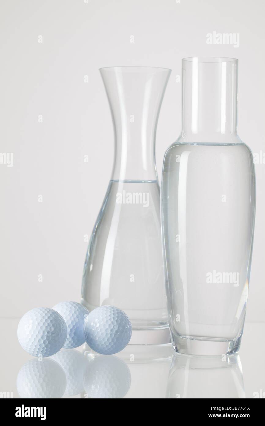 Zwei Vasen mit sauberem Wasser und Golfbälle auf einem Glastisch Stockfoto