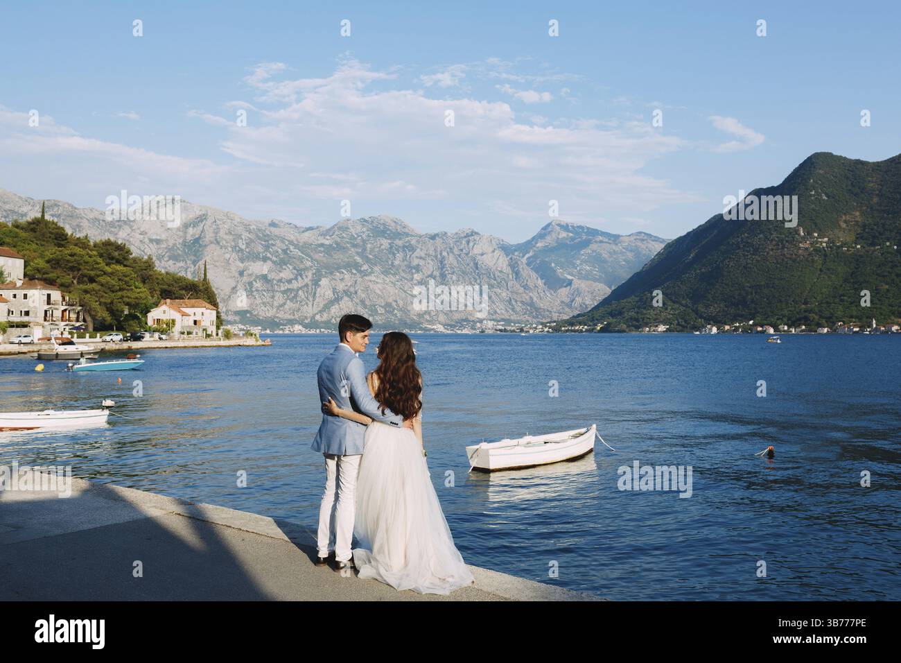 Die Braut und der Bräutigam, die sich am Pier in der Nähe der Altstadt von Perast umgibt, daneben befindet sich ein Boot. Stockfoto
