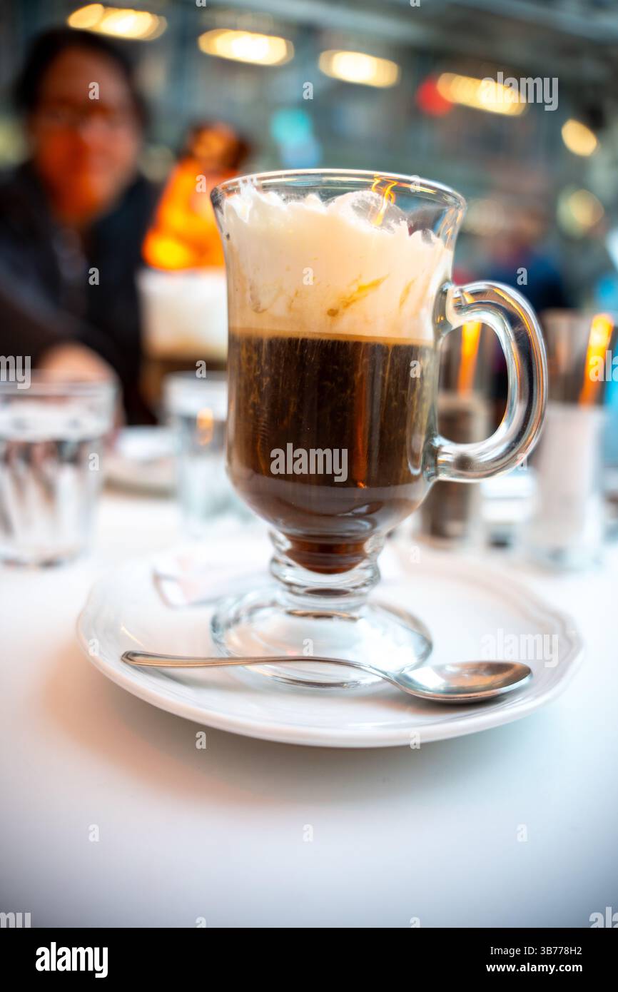 Nahaufnahme eines frisch servierten Wiener Kaffees mit Schlagsahne in einem klaren Glasbecher auf weißem Teller in einem stilvollen europäischen Café. Lifestyle visuell Stockfoto