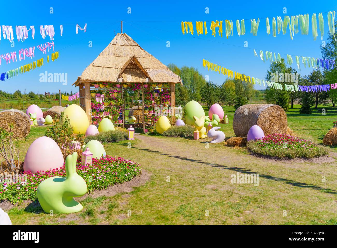 Lebendige Gartenanlage im Freien mit pastellfarbenen Ostereiern, dekorativen Elementen und einem Strohdach, perfekt für festliche Feiern. Stockfoto
