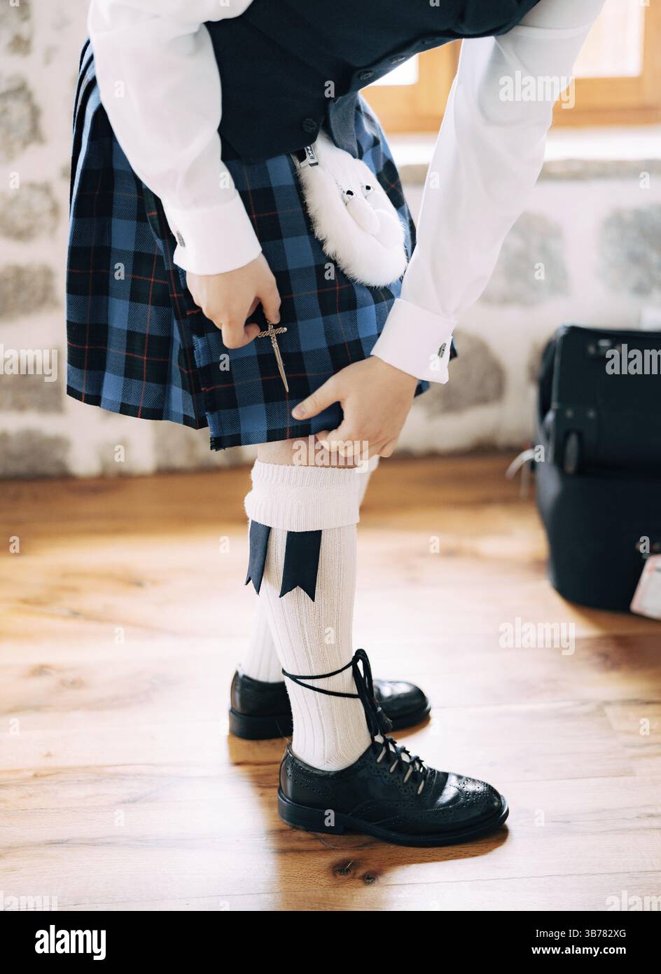 Vorbereitung auf eine schottische Hochzeit. Mann in hohen Socken, Sporran und Schuhen mit langen Schnürsenkeln befestigt ein kleines Schwert am Kilt. Stockfoto