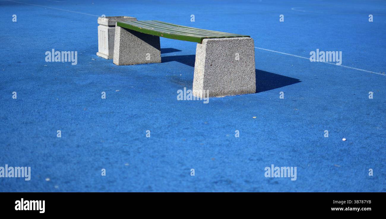 Blaues Sportfeld und leere Bank mit Mülleimer an sonnigem Tag Stockfoto