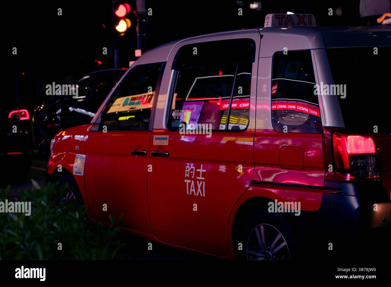 Ein rotes Hong Kong Taxi wartet unter dem Puls von Neonlichtern Stockfoto