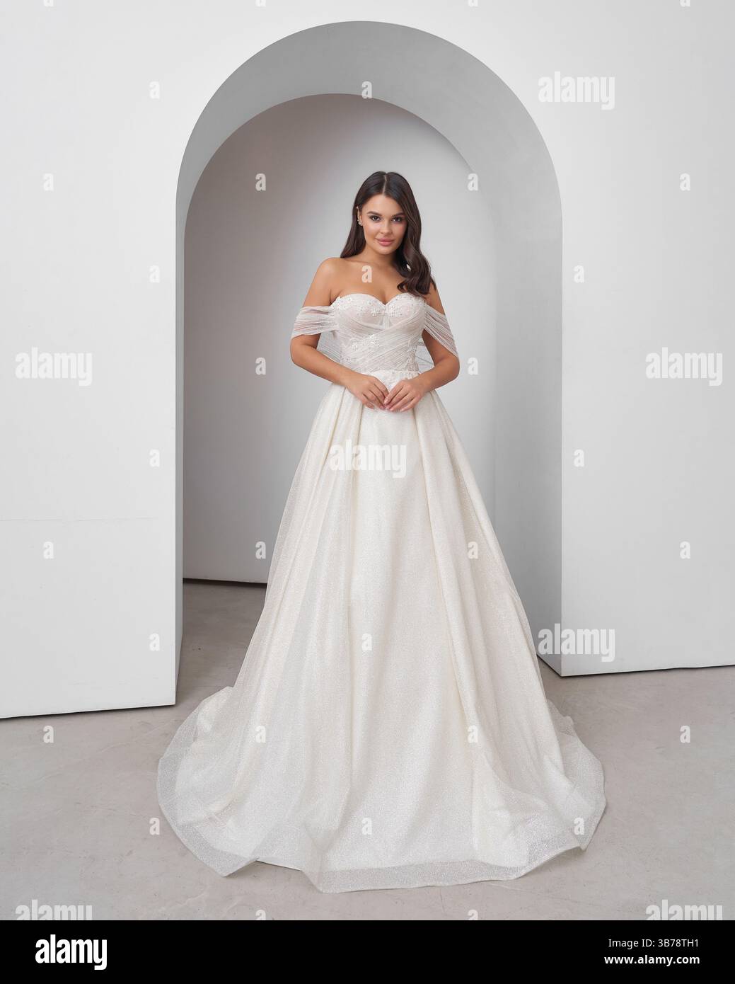 Brünette Frau im Hochzeitskleid posiert anmutig in heller Inneneinrichtung Stockfoto