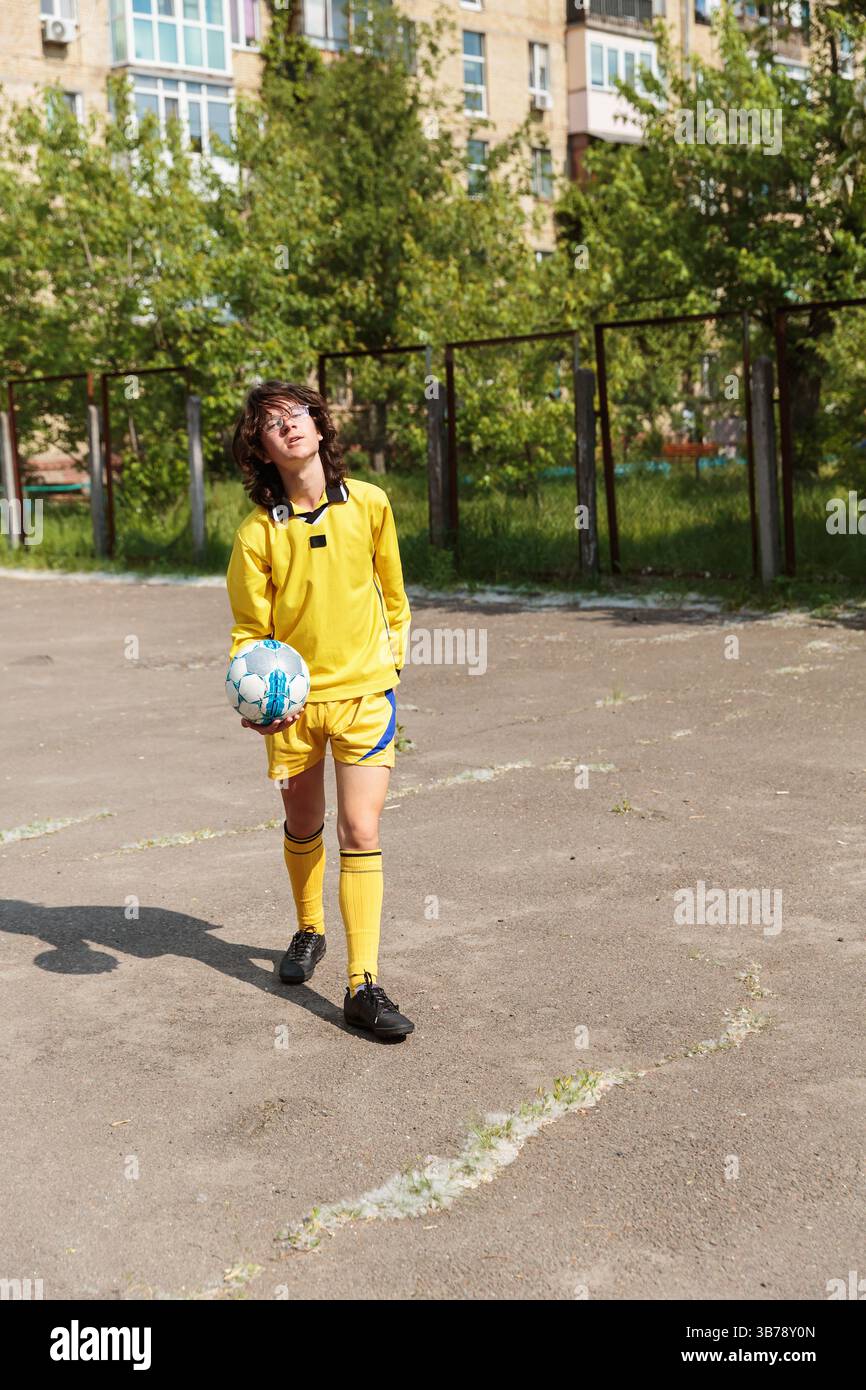 Jugendfußballer, der mit Ball auf dem Straßenplatz läuft Stockfoto