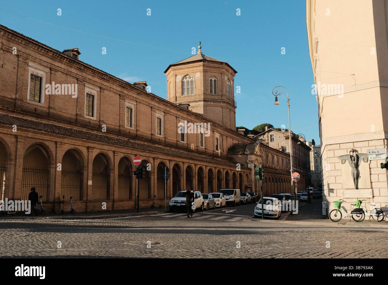 Kopfsteinpflasterstraße in der Nähe des Vatikans mit alten römischen Gebäuden, warmen Sonnenlicht, Fußgängern und klassischer italienischer Architektur in morgendlicher Stadtatmosphäre. Hochwertige Fotos Stockfoto