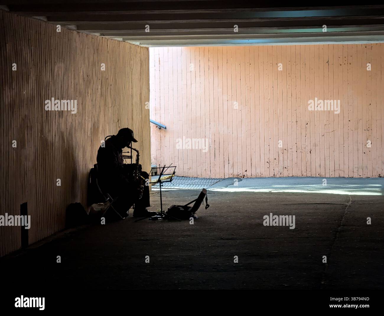 Ein Straßenmusiker spielt das Saxophon in einem schwach beleuchteten unterirdischen Gang. Das Echo der Musik füllt den Tunnel und erzeugt einen stimmungsvollen und atmosphärischen urb Stockfoto