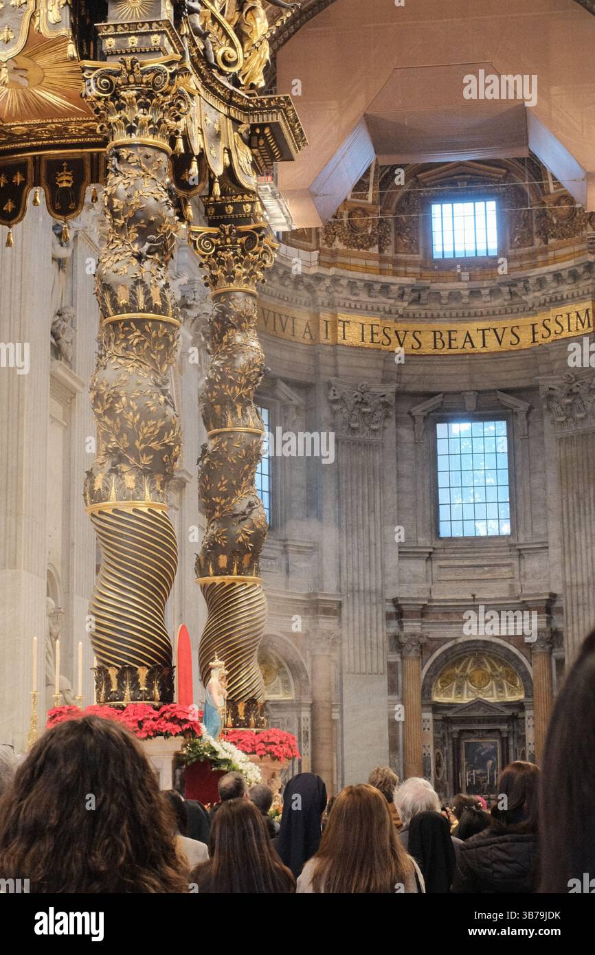 Verziertes Baldachin-Baldachin über dem Papstaltar in der Petersbasilika Vatikanstadt, entworfen von Gian Lorenzo Bernini, mit verdrehten Bronzesäulen, roten Blumendekorationen und lateinischen Inschriften unter der großen Kuppel. Hochwertige Fotos Stockfoto