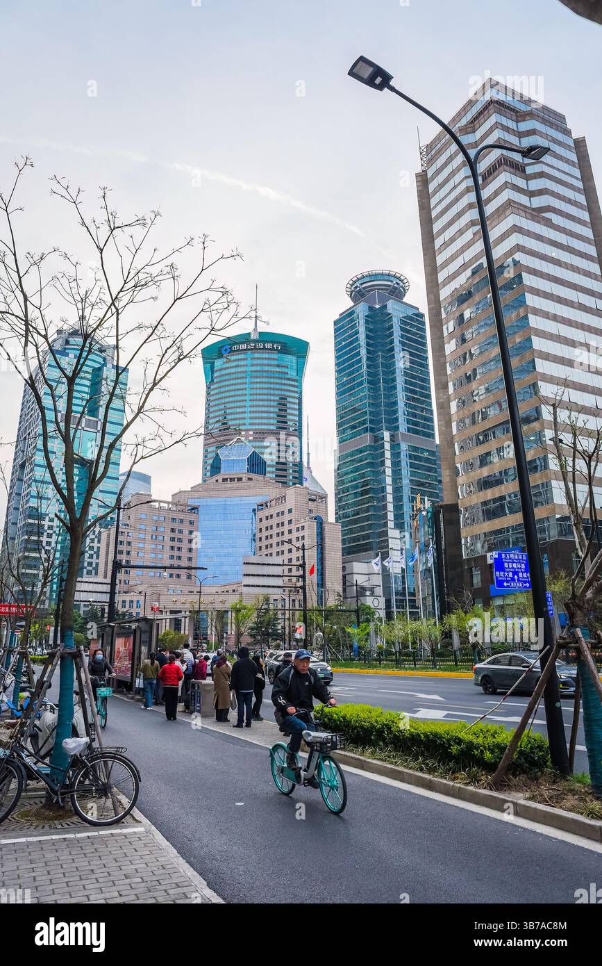 Shanghai, China - 1. April 2025: Abendliche Straßenszene in Pudong mit Menschen, Radfahrern und modernen Wolkenkratzern unter weichem Himmel, die urbane Touris zeigt Stockfoto