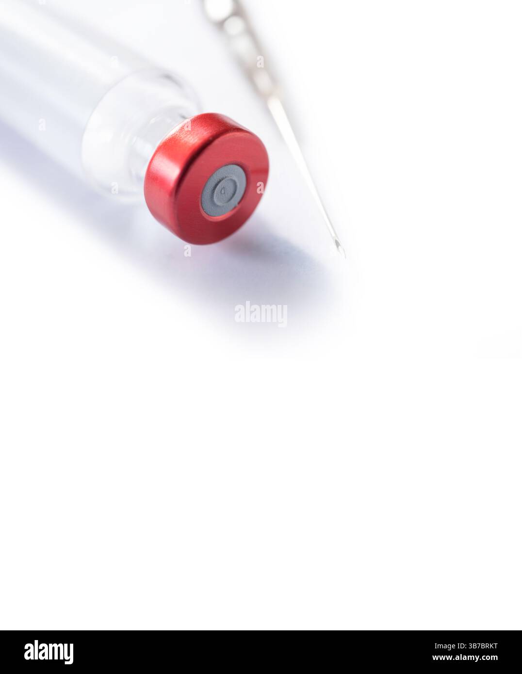 Die dünne Spritze liegt neben einer Impfflasche mit rotem Verschluss auf weißem Hintergrund. Platz für Text und Design Stockfoto