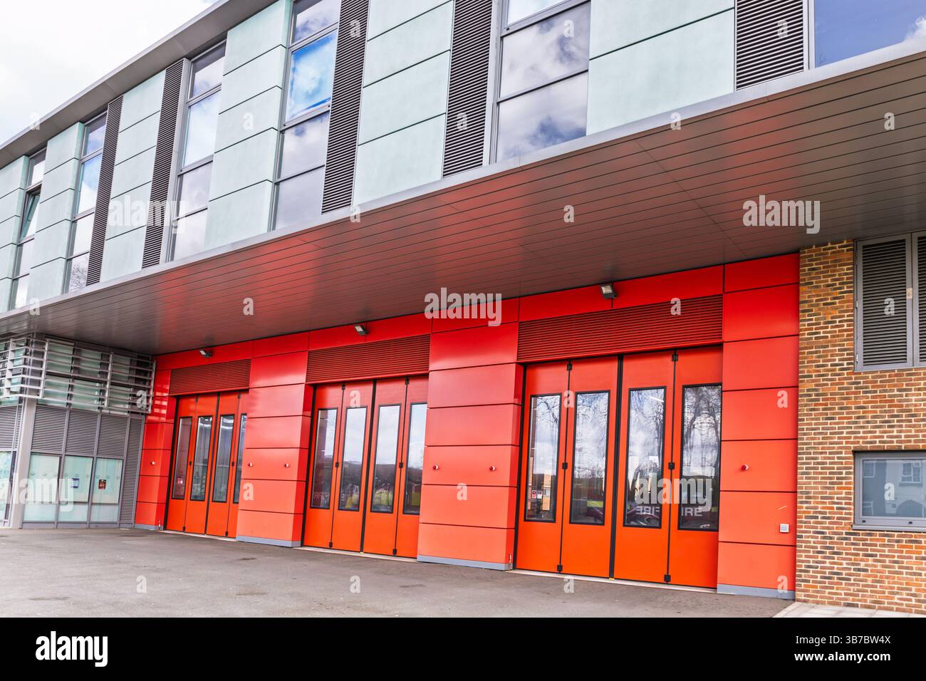 Hellrote Feuerwehrtüren in einem modernen Backsteingebäude mit Glasfenstern Stockfoto