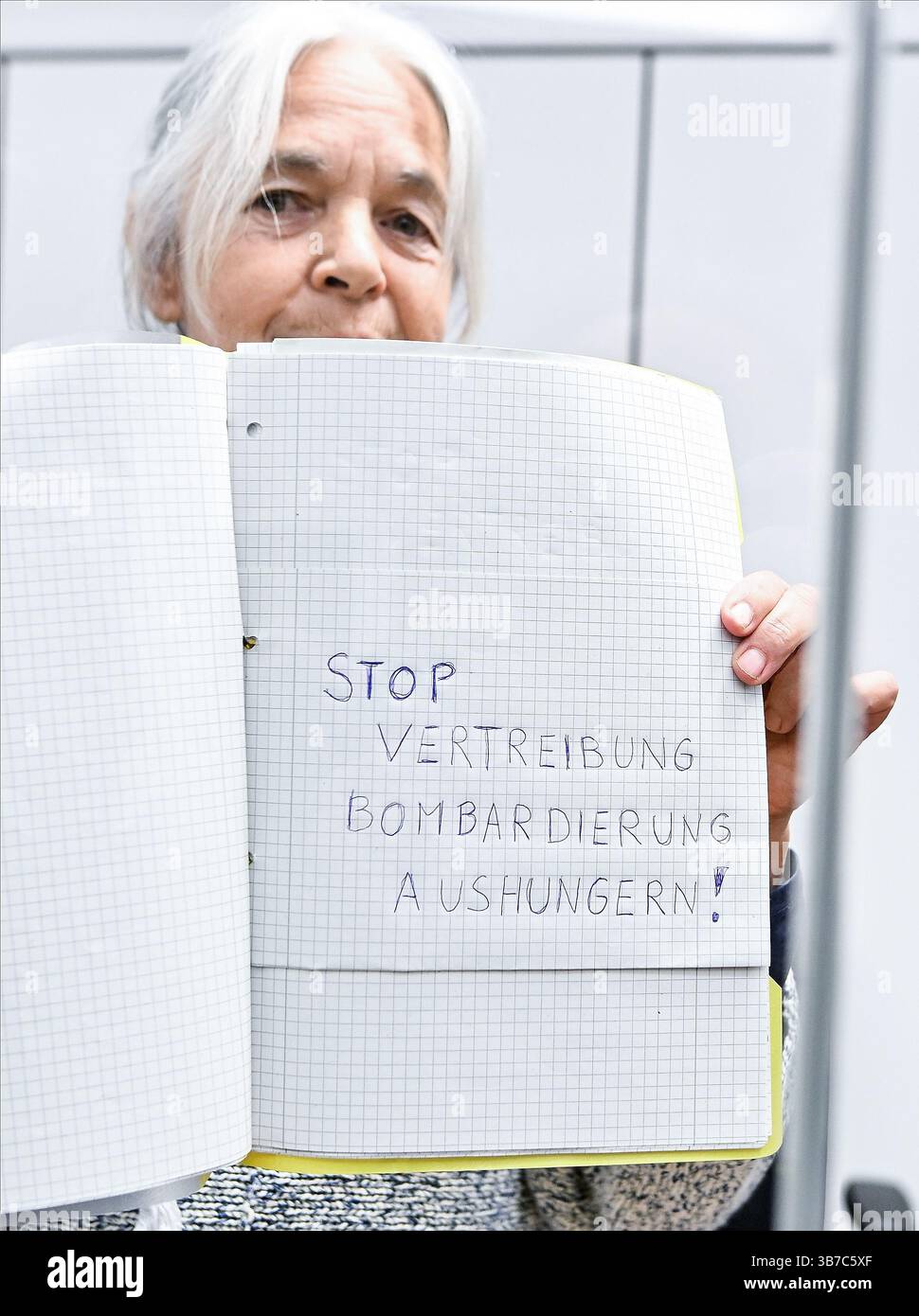 6. Mai 2025, Niedersachsen, Celle: Daniela Klette, ehemaliges Mitglied der militanten deutschen Linksextremistengruppe Rote Armee Fraktion (RAF), zeigt eine Aufschrift mit der Aufschrift „Stop Displacement Bombing Hungervation!“ An einem weiteren Tag des Verfahrens vor dem Oberlandesgericht Celle. Klette war Mitglied der „dritten Generation“ der Roten Armee-Fraktion, einer linken Terrorgruppe, die für politisch motivierte Morde, Entführungen und Angriffe in den 1980er und 90er Jahren sowie für Supermarkt- und Transitüberfälle in den 2000er Jahren verantwortlich war In diesem Prozess wird sie wegen bewaffneten Raubs angeklagt. Zwei Stockfoto