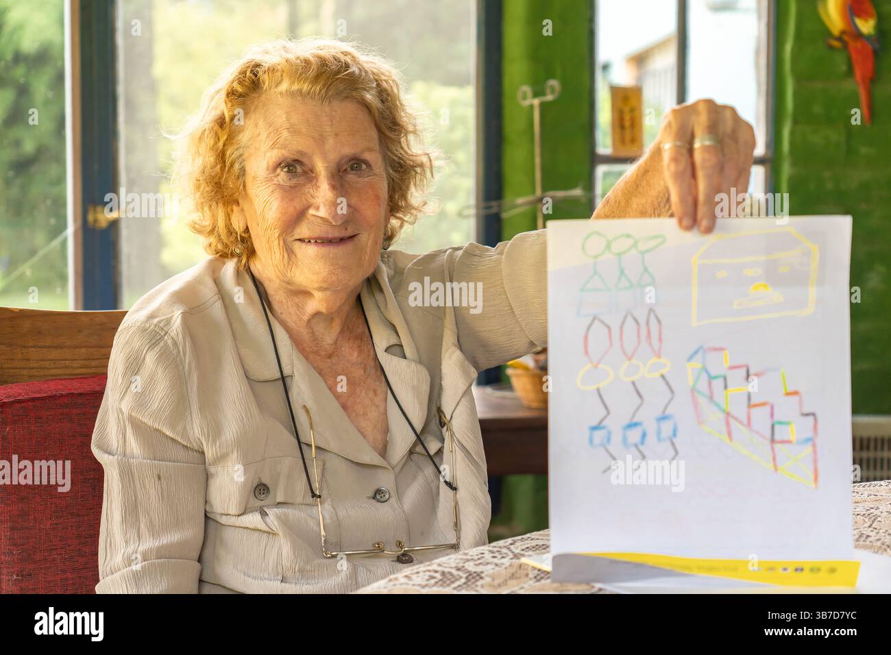 Glückliche Großmutter zeigt stolz eine farbenfrohe Zeichnung ihres Enkelkindes und genießt einen herzerwärmenden Moment der Verbundenheit und Kreativität in einer gemütlichen Atmosphäre Stockfoto