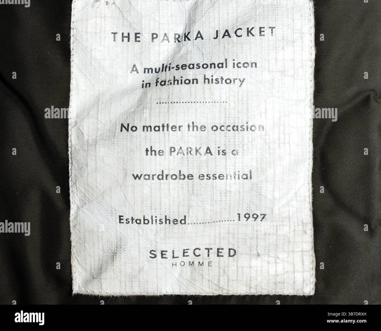 Ausgewähltes Homme Parkajacke-Label mit Werbetext, der das Kleidungsstück als unverzichtbares Kleidungsstück und vielseitiges Kleidungsstück für mehrere Jahreszeiten unterstreicht Stockfoto