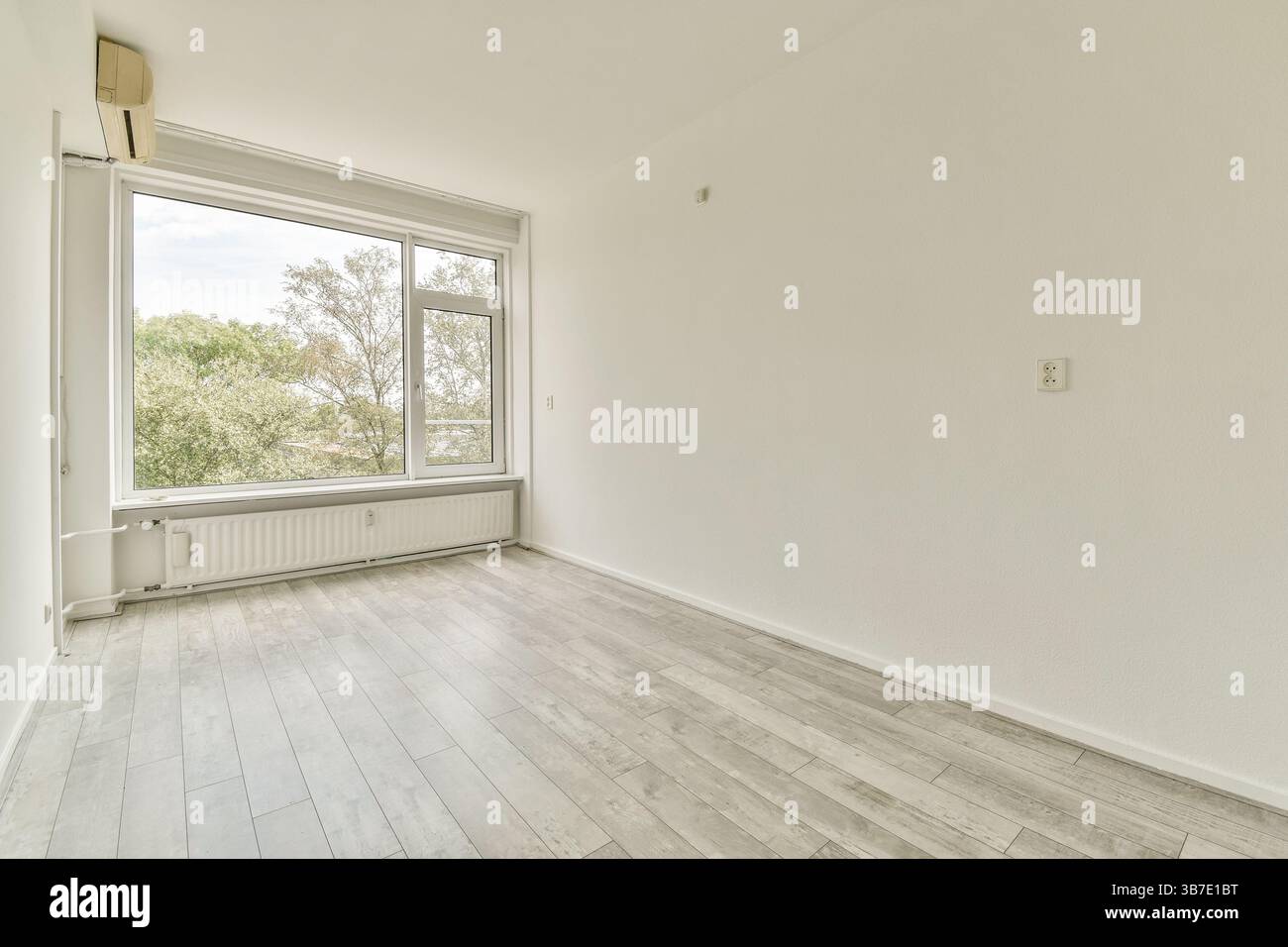 Ein geräumiger, übersichtlicher Raum mit großen Fenstern, die den Raum mit natürlichem Licht durchfluten, mit hellem Holzboden und neutralen Wänden. Stockfoto