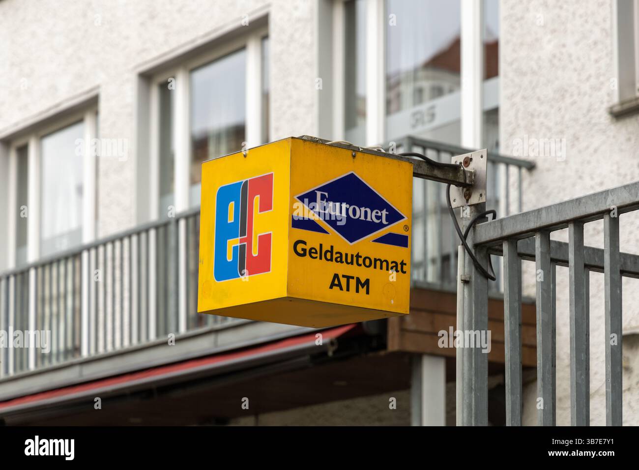 Nahaufnahme eines gelben Euronet ATM-Schilds mit EC-Logo auf einer Straße in Deutschland, montiert auf einem Metallmast vor einem Wohngebäude im Hintergrund. B Stockfoto