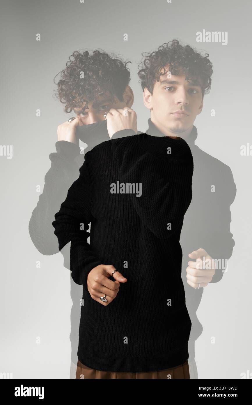 Ein hübscher Mann mit lockigen Haaren präsentiert ein trendiges Outfit vor minimalistischer Kulisse. Stockfoto