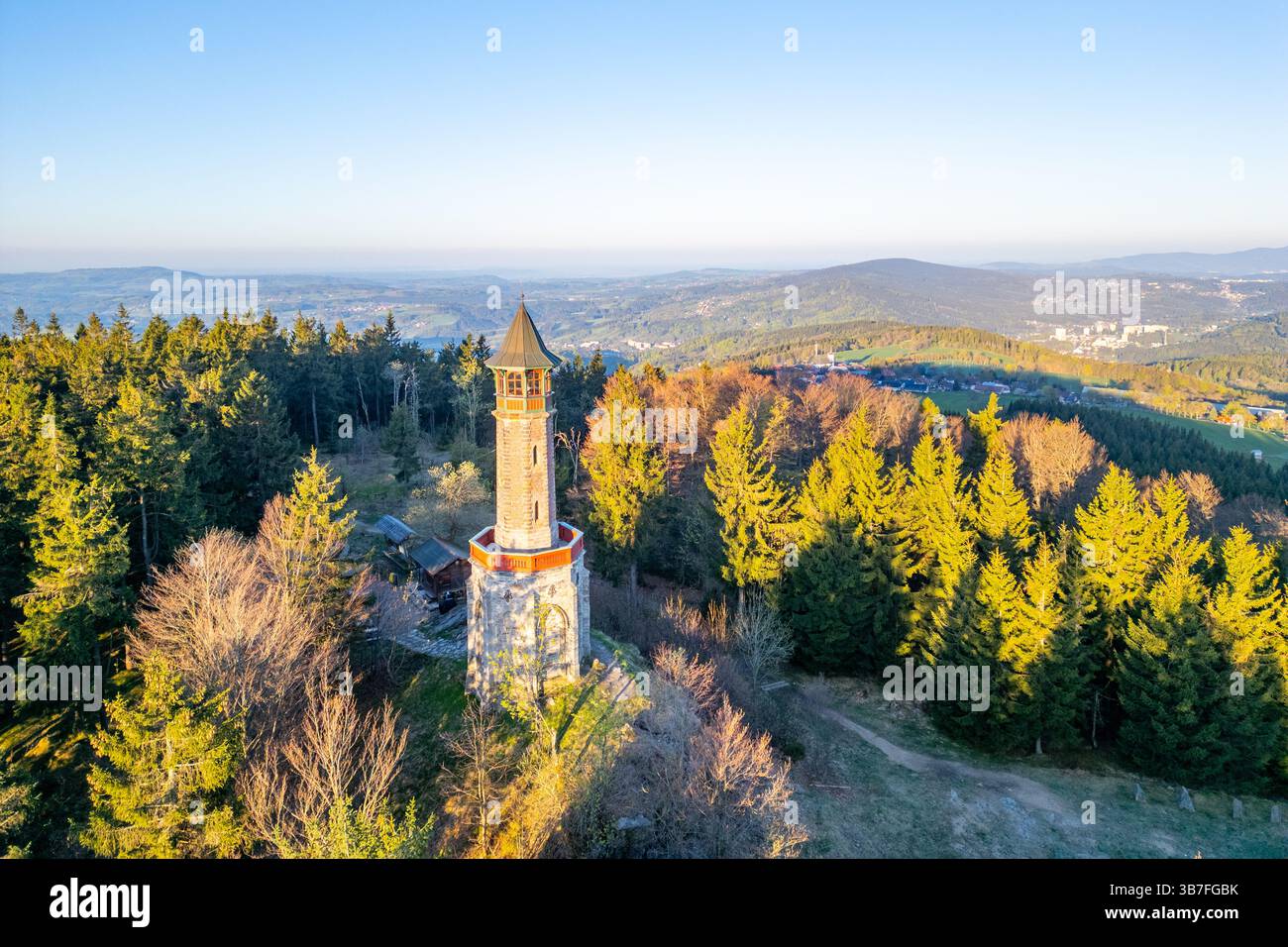An einem ruhigen Frühlingsmorgen steht der Stepanka Aussichtsturm hoch inmitten üppiger grüner Bäume in Korenov und bietet einen weiten Blick auf das Isergebirge und die umliegende Landschaft. Stockfoto
