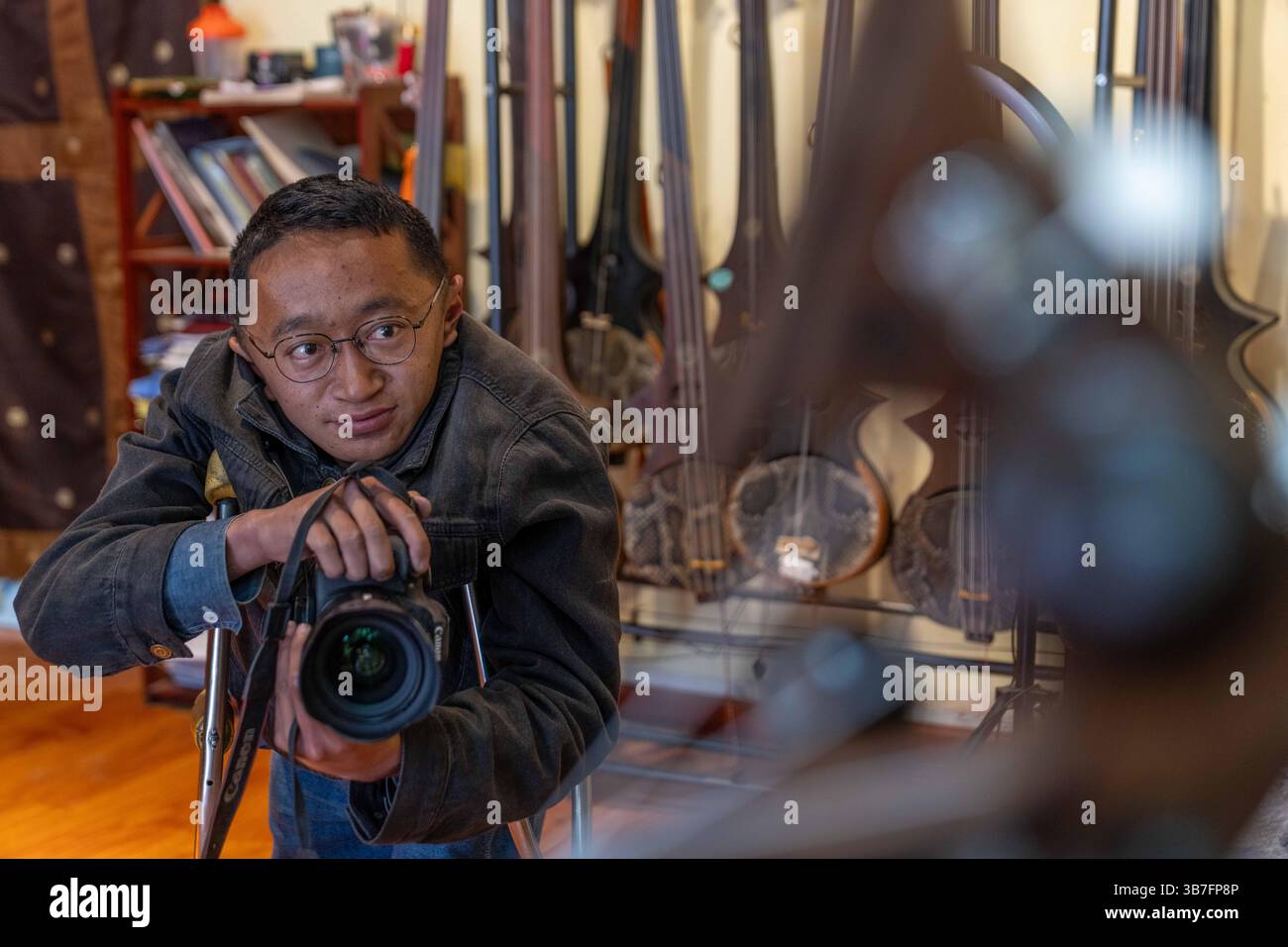 (250506) -- LHASA, 6. Mai 2025 (Xinhua) -- Lhapa Dondrup fotografiert das Zhanian, ein traditionelles tibetisches Streichinstrument, bei der Firma in Lhasa, südwestchinesischer Autonomen Region Xizang, 6. Mai 2025. Lhapa Dondrup, ein 24-jähriger Mann, der in Lhasa geboren wurde, leidet seit seiner Kindheit an Osteogenesis imperfecta (OI), allgemein bekannt als brüchige Knochenerkrankung. Als Erwachsener steht er unter einem Meter groß und verlässt sich auf Krücken und elektrischen Rollstuhl für Mobilität. Trotz dieser Herausforderungen träumt Lhapa davon, Fotograf zu werden. 2021 wechselte er zu einem Kulturmedienunternehmen Stockfoto