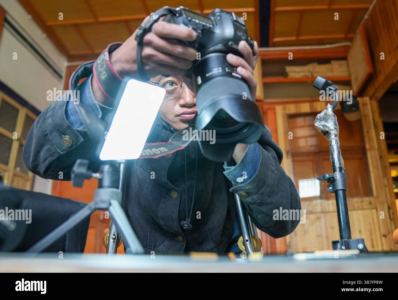(250506) -- LHASA, 6. Mai 2025 (Xinhua) -- Lhapa Dondrup fotografiert ein Produkt bei der Firma in Lhasa, südwestchinesischer Autonomen Region Xizang, 5. Mai 2025. Lhapa Dondrup, ein 24-jähriger Mann, der in Lhasa geboren wurde, leidet seit seiner Kindheit an Osteogenesis imperfecta (OI), allgemein bekannt als brüchige Knochenerkrankung. Als Erwachsener steht er unter einem Meter groß und verlässt sich auf Krücken und elektrischen Rollstuhl für Mobilität. Trotz dieser Herausforderungen träumt Lhapa davon, Fotograf zu werden. 2021 schloss er sich einem Kulturmedienunternehmen an, das von Menschen mit körperlicher Behinderung gegründet wurde Stockfoto